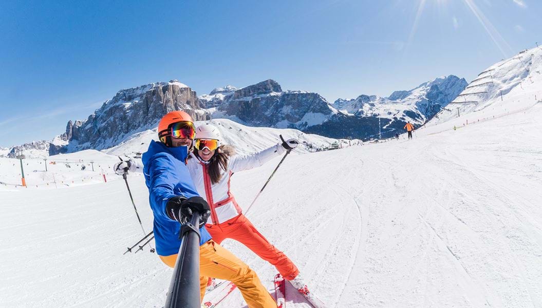 Glade skiløbere på pisten med udsigt over bjergtoppe i Canazei